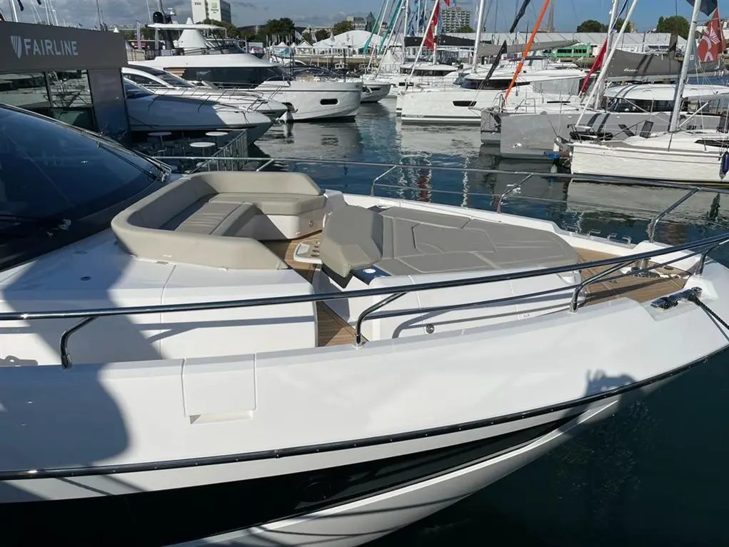 Modern motorboat with a spacious deck and seating area, docked at a marina surrounded by various yachts.